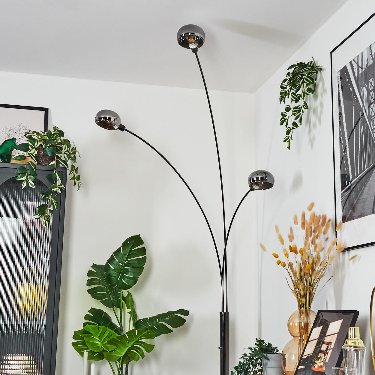 Modernes Wohnzimmer mit schwarzer Stehlampe mit drei Kugelleuchten. Pflanzen und Bilder dekorieren den Raum.