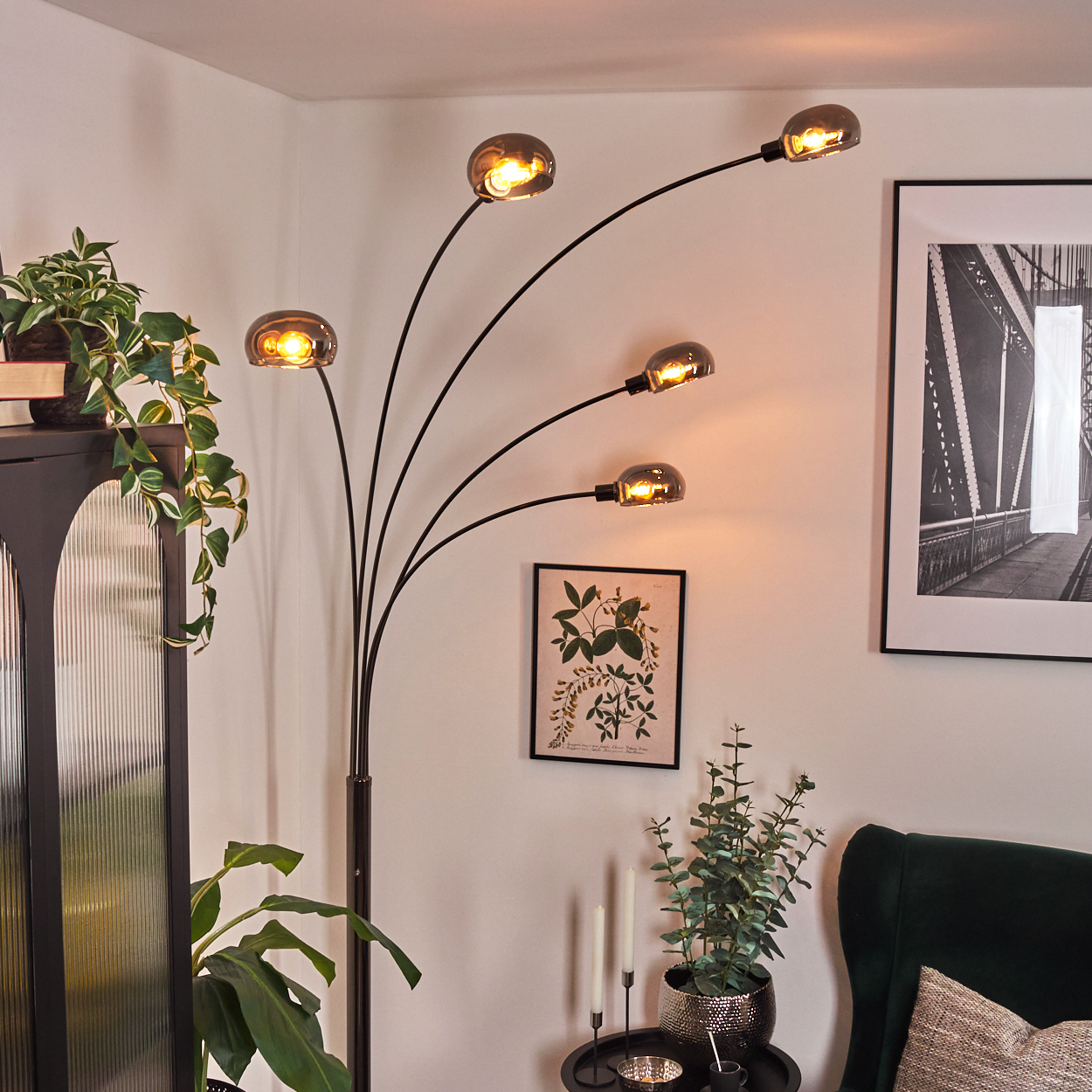 Ein modernes Wohnzimmer mit schwarzer Stehlampe, Pflanzen, Schrank, grünem Sessel und gerahmter Kunst.