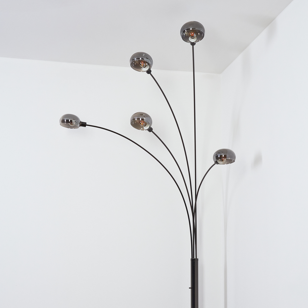 Moderne schwarze Stehlampe mit fünf kugelförmigen Lichtern. Sie steht in einer weißen Zimmerecke.