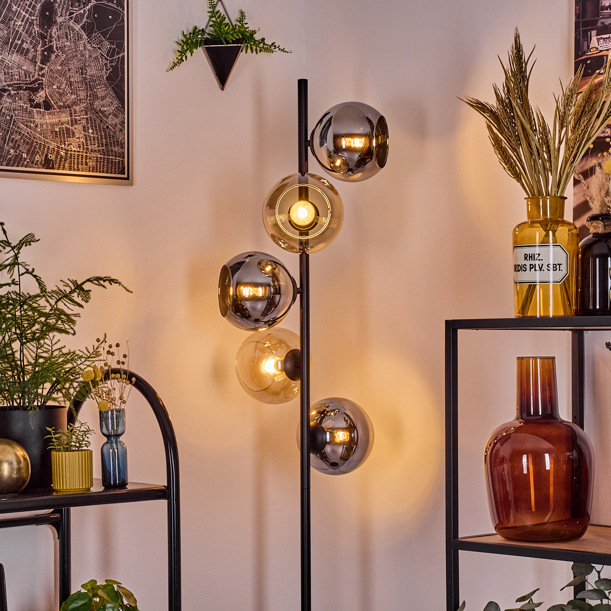 Eine moderne Stehlampe mit Glaskugeln, Pflanzen und Regalen mit Vasen im Raum. Eine Karte hängt an der Wand.