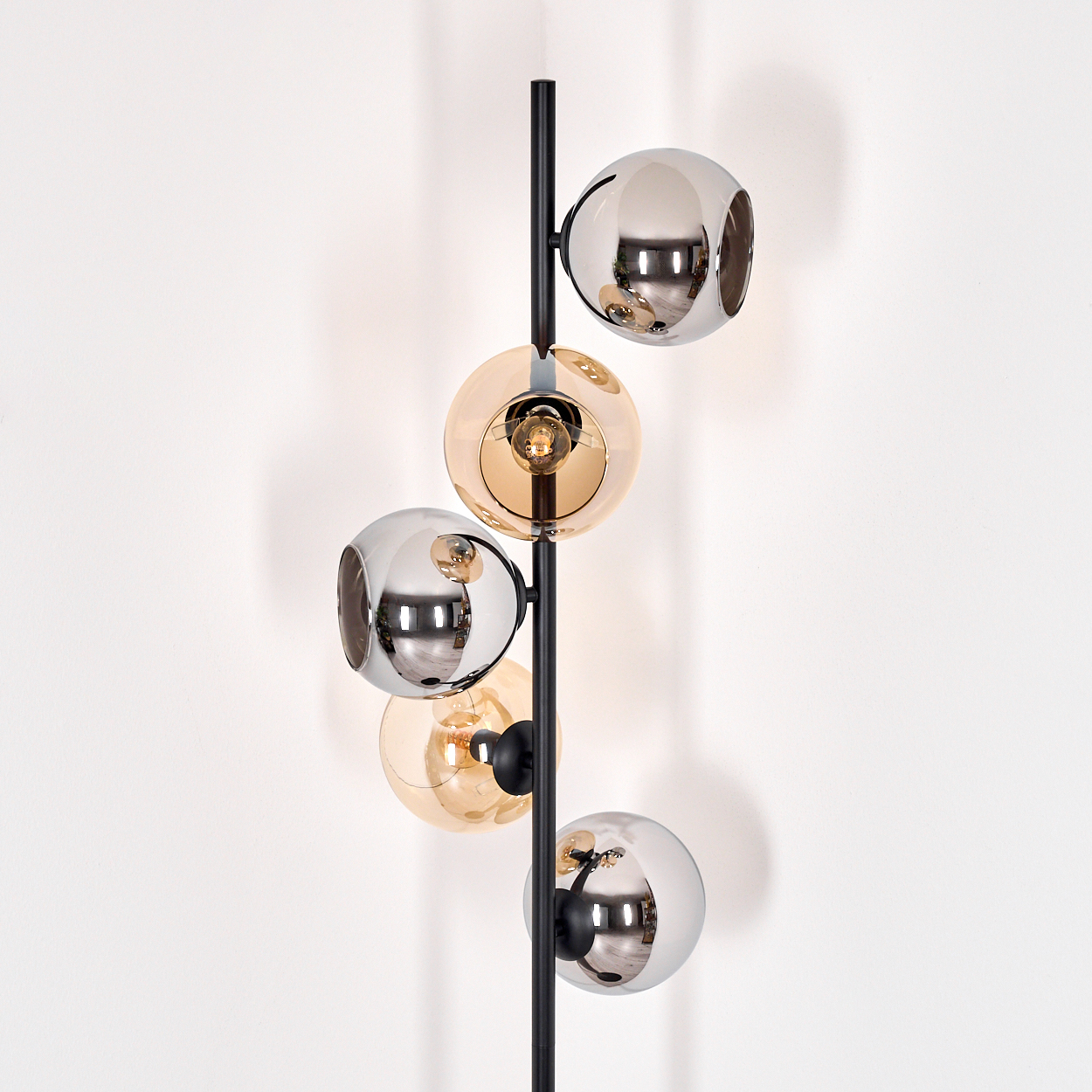 Moderne Stehlampe mit schwarzem Pfosten und fünf kugelförmigen Lampenschirmen in Chrom- und Bernsteinfarben vor weißer Wand.