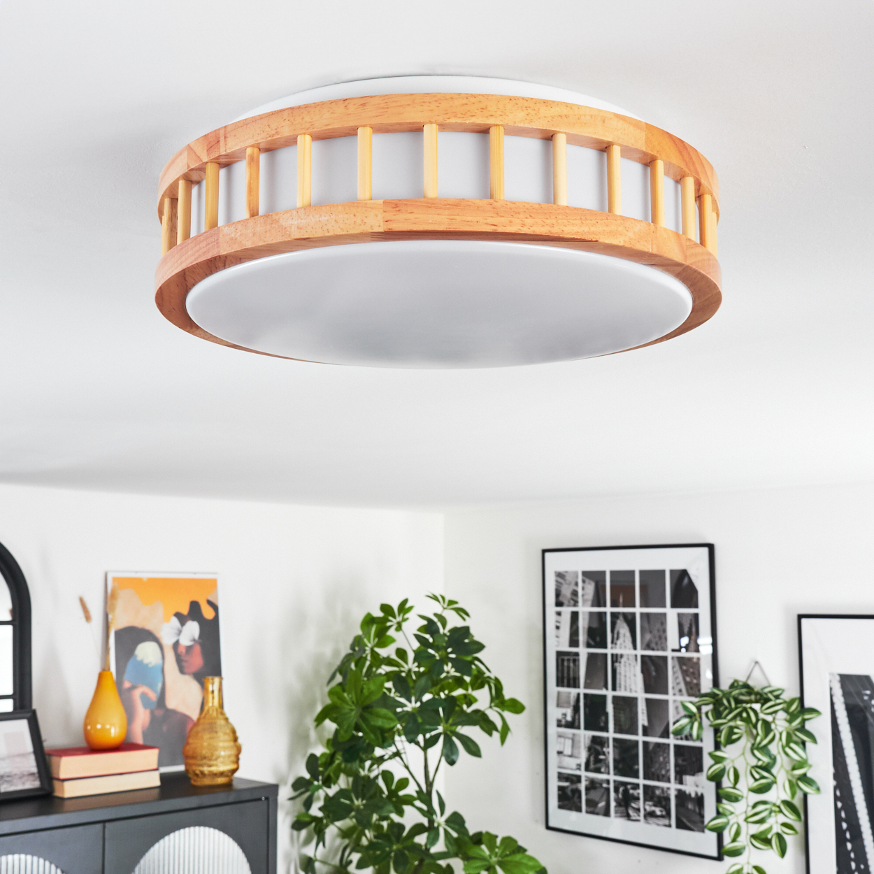 Moderne Deckenlampe mit Holzrahmen und weißer Abdeckung. Der Raum hat Kunst, Pflanzen und einen schwarzen Schrank.