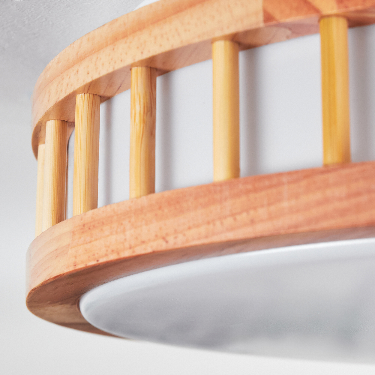 Nahaufnahme einer Holzleuchte. Sie hat einen hellen Holzrahmen mit vertikalen, zylindrischen Stützen und einem weißen, abgerundeten Diffusor.