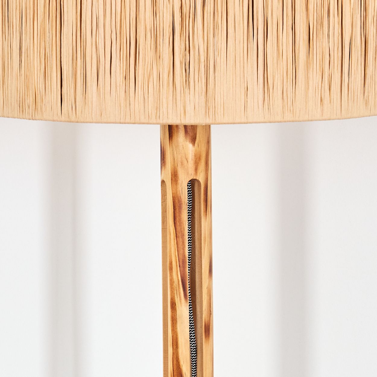 Nahaufnahme einer Lampe. Der Lampenschirm ist beige, die Holzstange hellbraun mit einem schwarz-weißen Kabel.