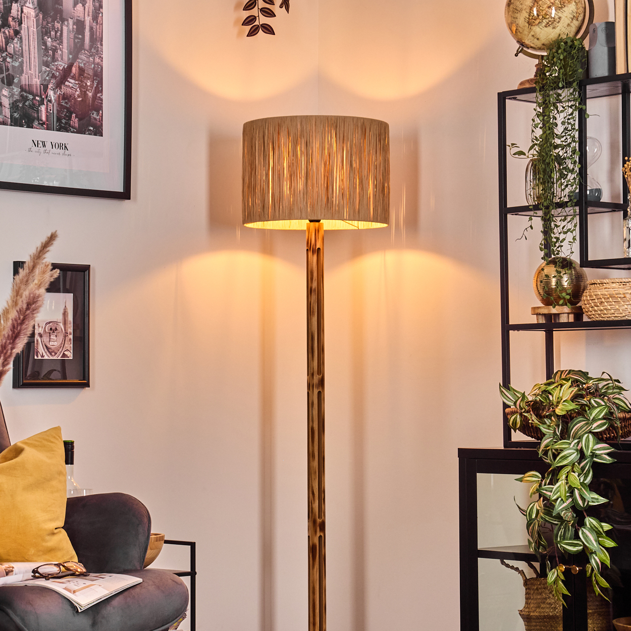 Eine beleuchtete Stehlampe steht in einem Raum mit Regal, Stuhl und Dekoration, darunter ein New York-Druck und ein Globus.
