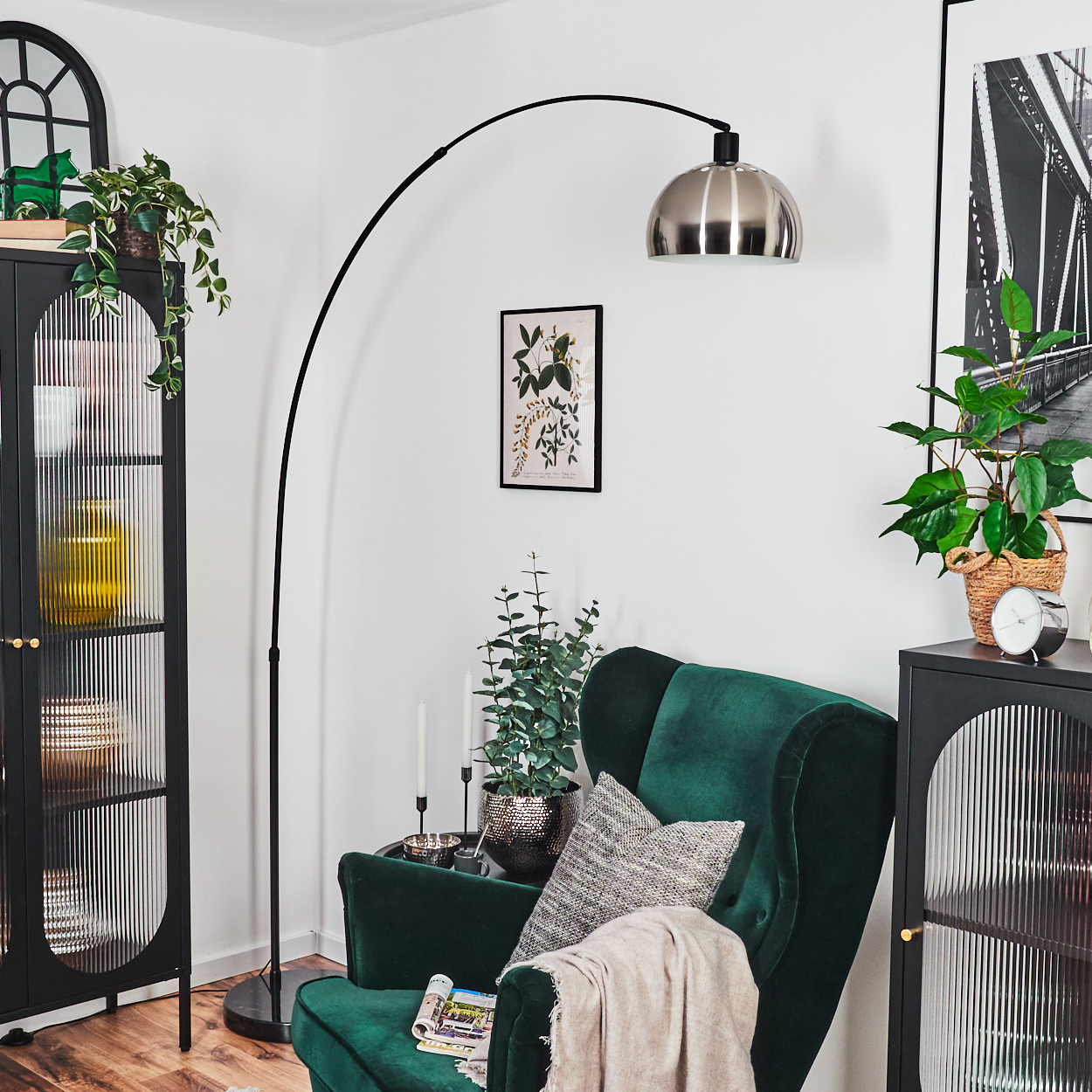 Ein grüner Sessel mit Decke, eine Stehlampe, ein Bild, Pflanzen in Töpfen und ein schwarzer Schrank befinden sich in einem hellen Raum.