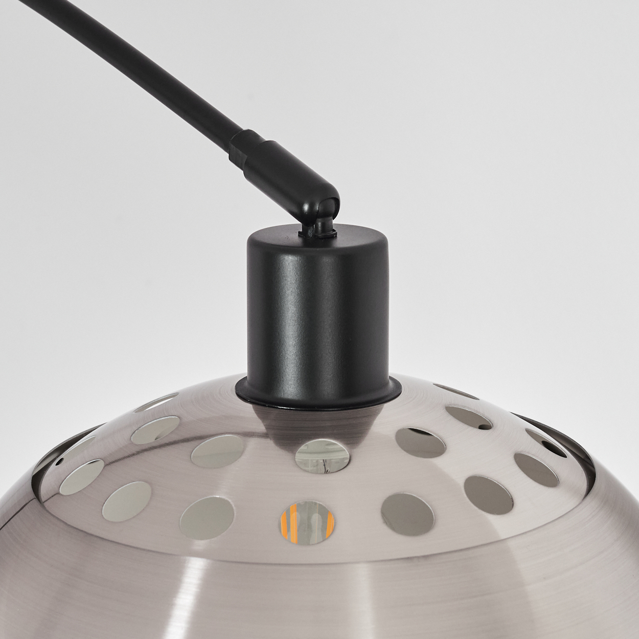 Nahaufnahme einer silbernen Lampe mit schwarzem Arm. Die Lampe hat einen perforierten Schirm und einen schwarzen zylindrischen Sockel.