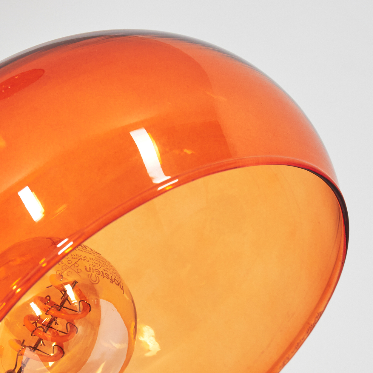 Nahaufnahme einer orangefarbenen Glaslampe. Die Lampe hat eine Glühbirne im Inneren. Der Hintergrund ist weiß.