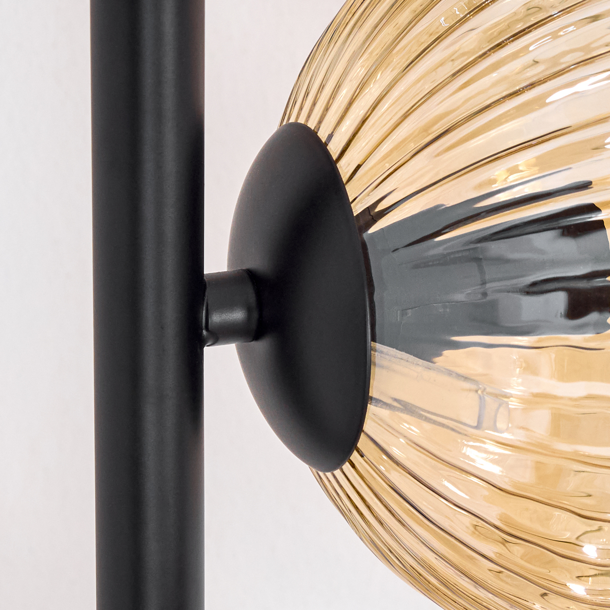 Nahaufnahme einer Lampe mit schwarzem Ständer und gelb getöntem Glasschirm. Der Schirm hat ein geripptes Muster.