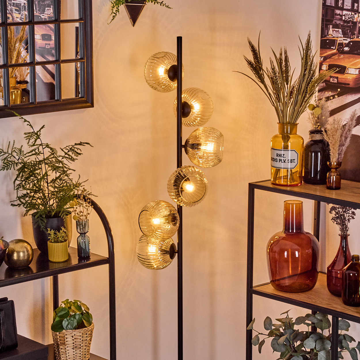 Ein modernes Wohnzimmer mit einer schwarzen Stehlampe mit Glaskugeln, Regalen mit Vasen und Pflanzen und einem Fenster.