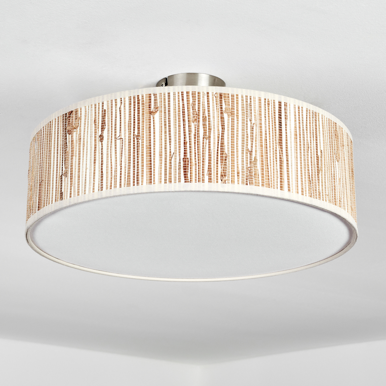 Eine Deckenlampe mit zylindrischem Schirm aus gewebten Bambusstreifen. Der Boden ist weiß, die Oberseite metallisch.