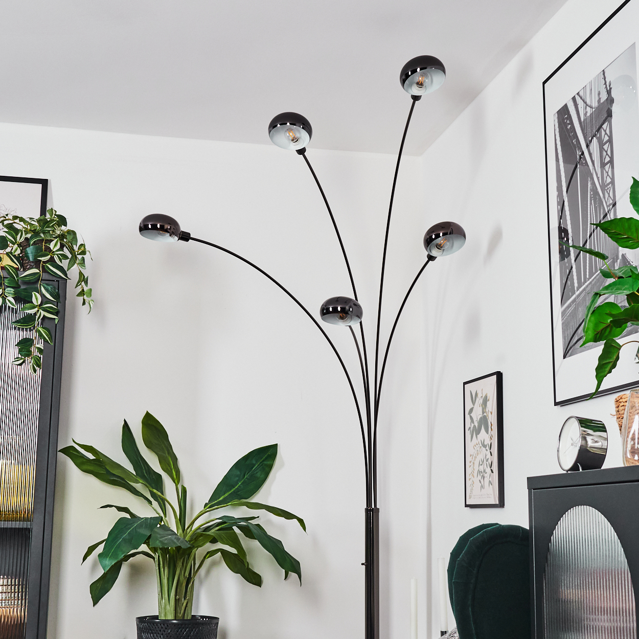 Ein modernes Wohnzimmer mit einer schwarzen Stehlampe mit fünf Glühbirnen. Es gibt eine grüne Pflanze und einen Bilderrahmen.