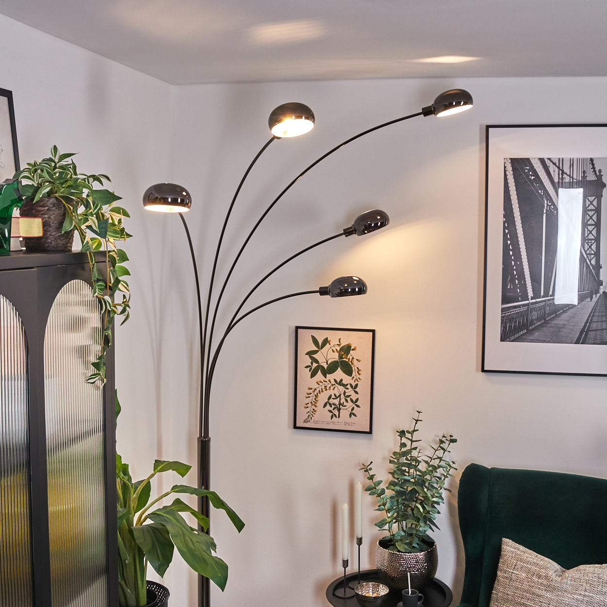 Ein modernes Wohnzimmer mit schwarzer Stehlampe, Pflanzen, Brückenbild und dunkelgrünem Sessel.