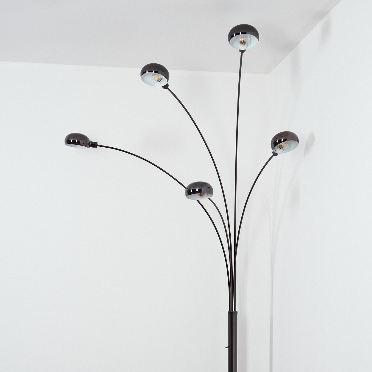 Eine moderne schwarze Stehlampe mit fünf gebogenen Armen, die jeweils eine runde Leuchte halten, vor einer weißen Wand.