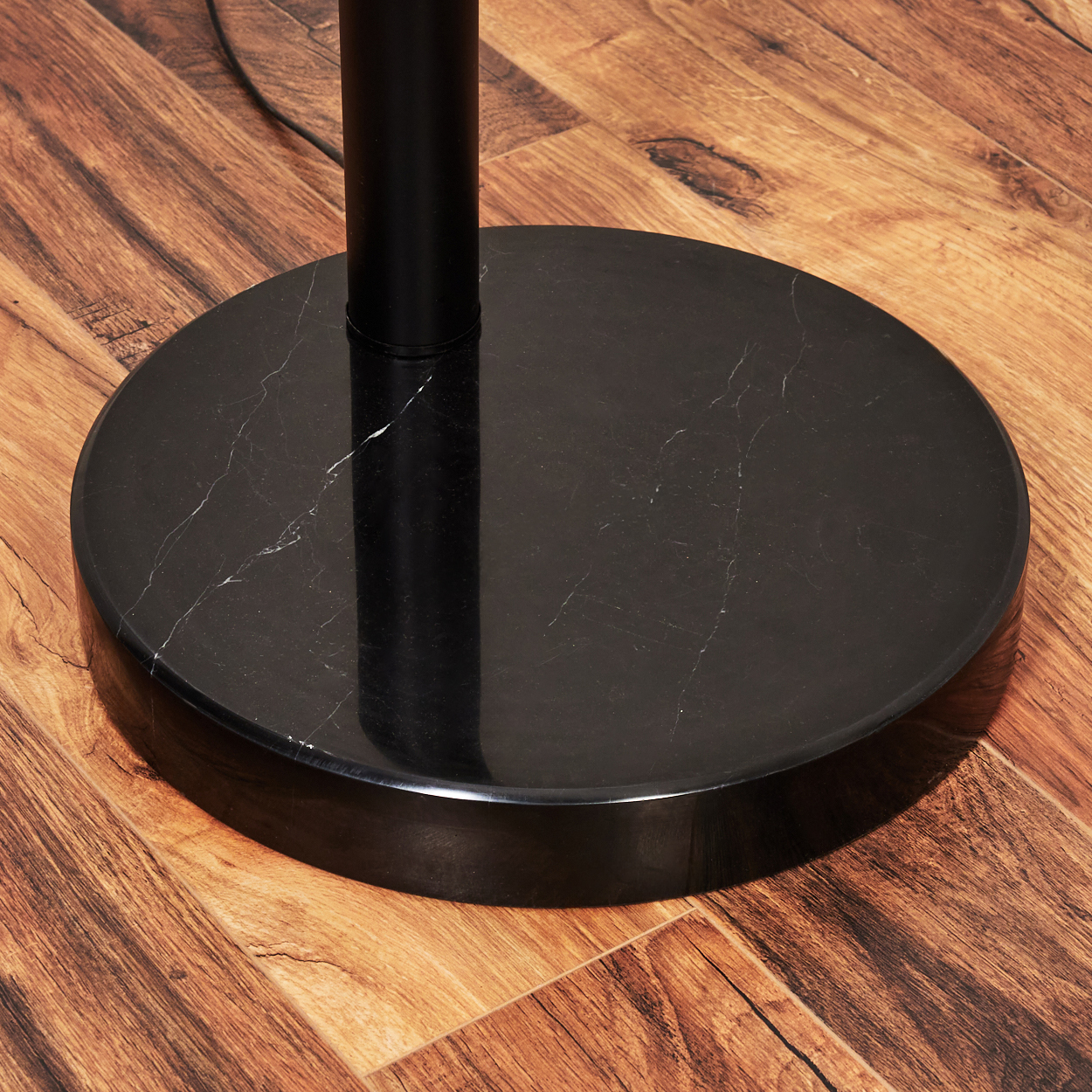 Nahaufnahme eines schwarzen Marmor-Lampenfußes auf einem Holzboden. Eine schwarze Stange ragt aus dem Sockel. Der Boden hat ein Holzmaserungsmuster.