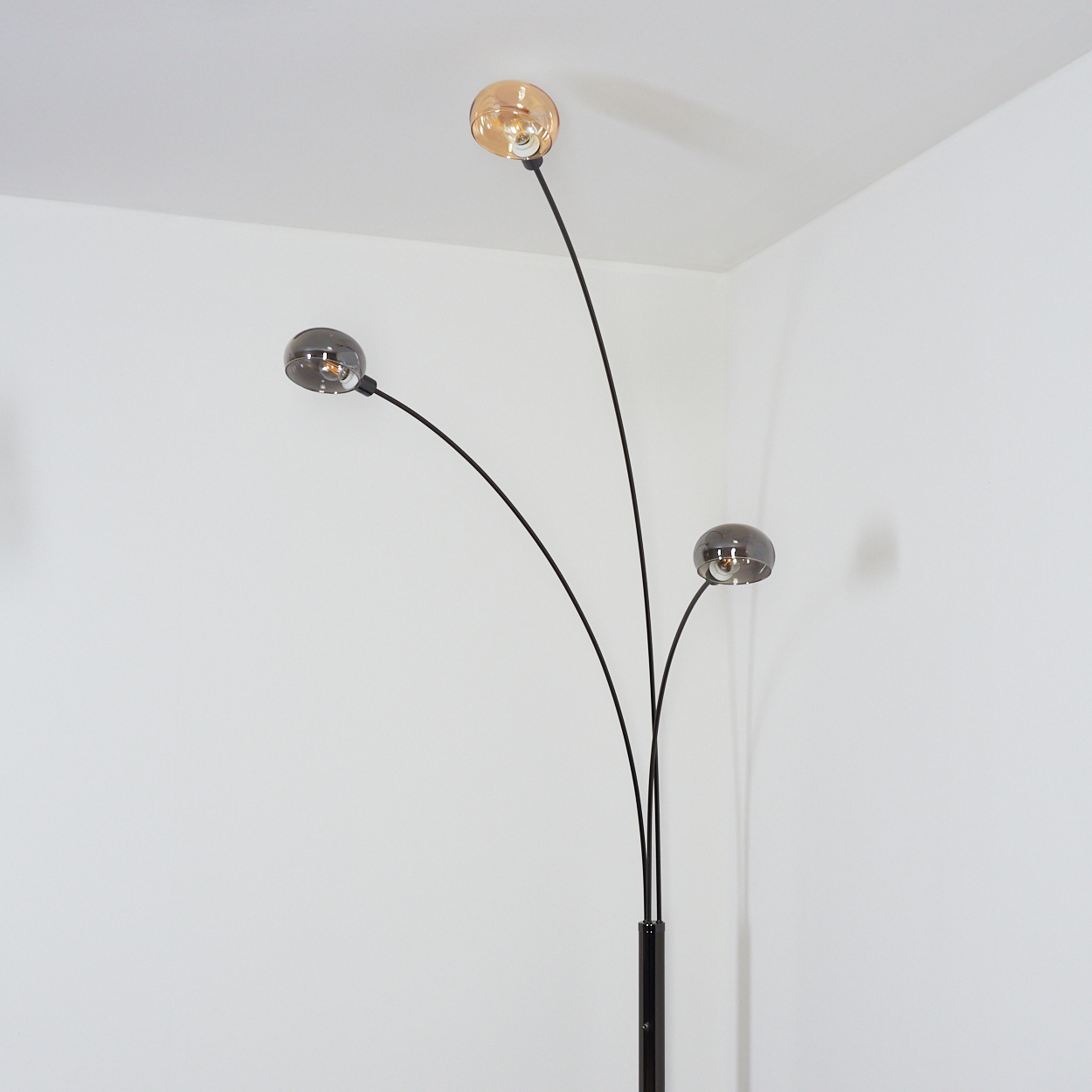 Eine moderne schwarze Stehlampe mit drei gebogenen Armen, die jeweils ein kugelförmiges Licht halten. Die Lampen haben bernsteinfarbene und graue Glasschirme.
