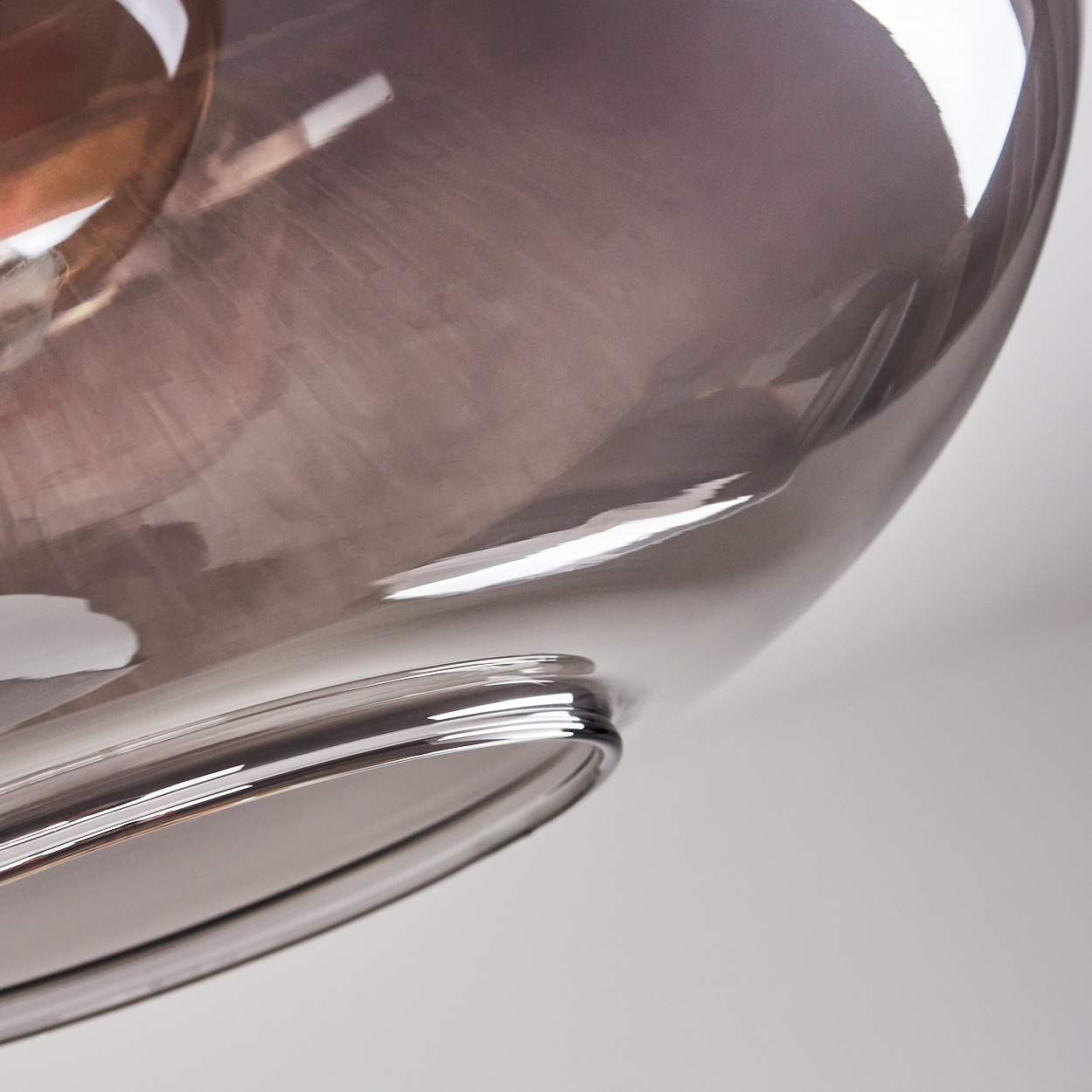 Nahaufnahme eines klaren Glasobjekts mit abgerundeter Form. Das Glas reflektiert Licht mit Braun- und Grautönen.