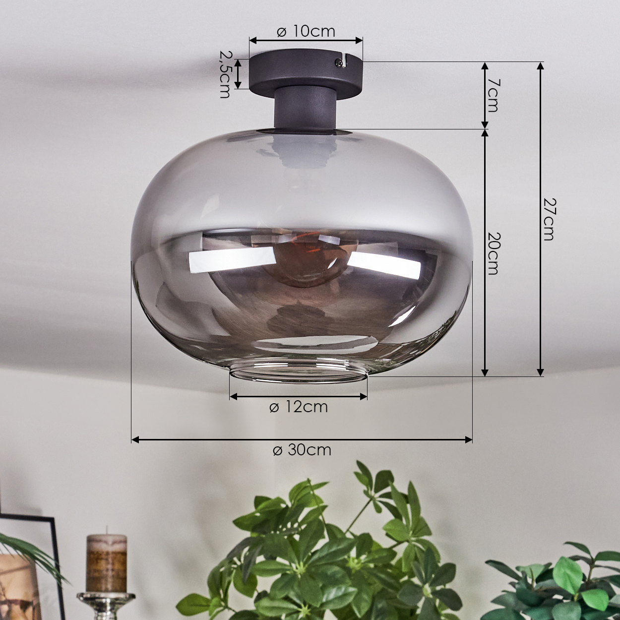 Eine Pendelleuchte mit rauchfarbenem Glasschirm, an einer weißen Decke montiert. Abmessungen sind mit schwarzen Linien angegeben. Grüne Pflanzen im Hintergrund.