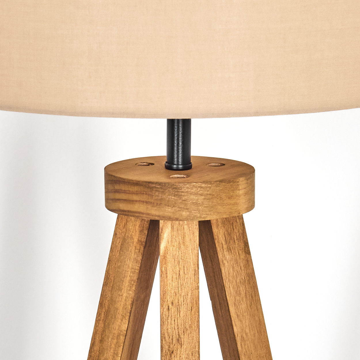 Nahaufnahme eines Holzlampensockels und eines beigefarbenen Lampenschirms. Die Lampe hat ein Stativ und eine schwarze Metallstütze. Weißer Hintergrund.