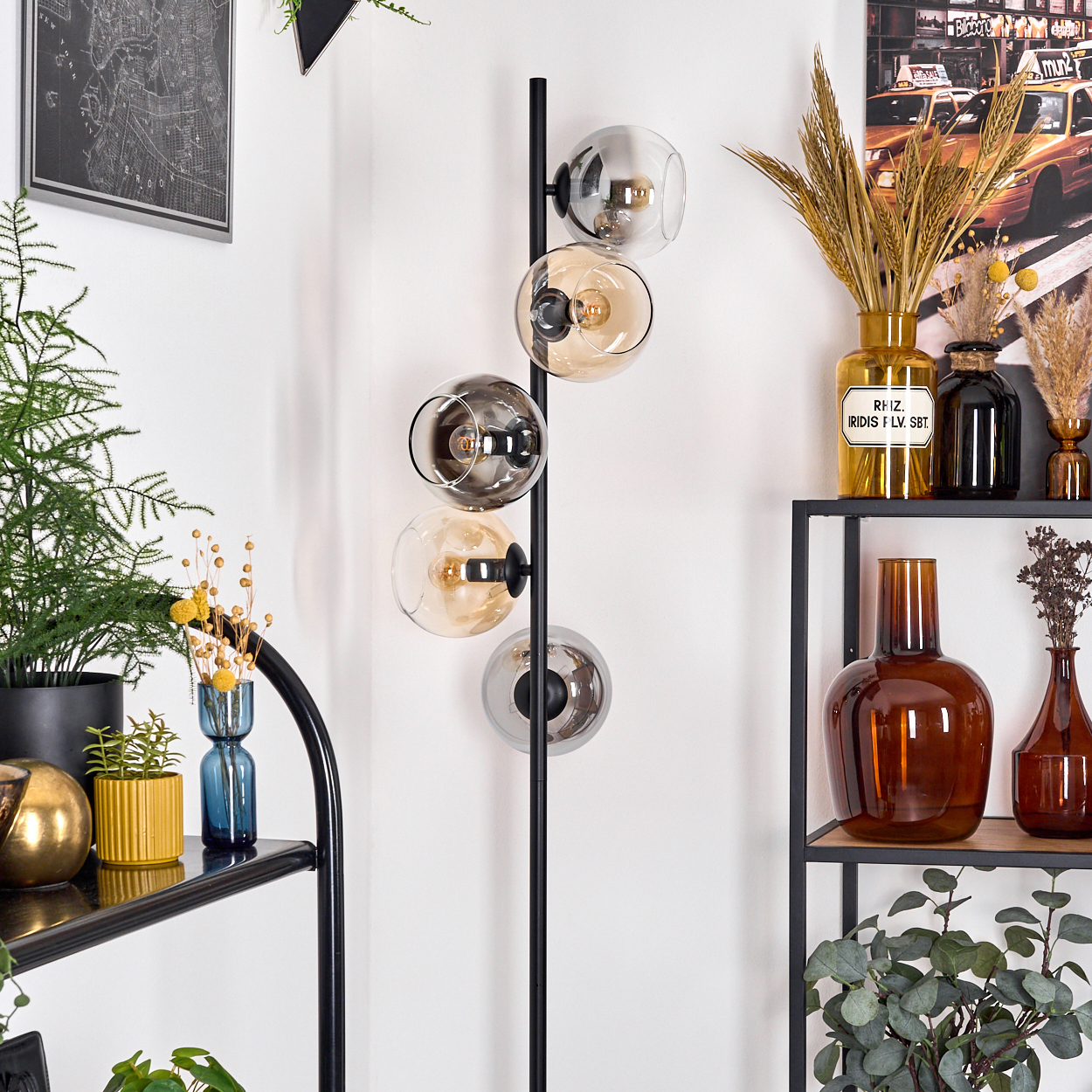 Eine moderne Lampe mit Glaskugeln, umgeben von Pflanzen und dekorativen Vasen auf einem schwarzen Regal und einem Landkartenbild.