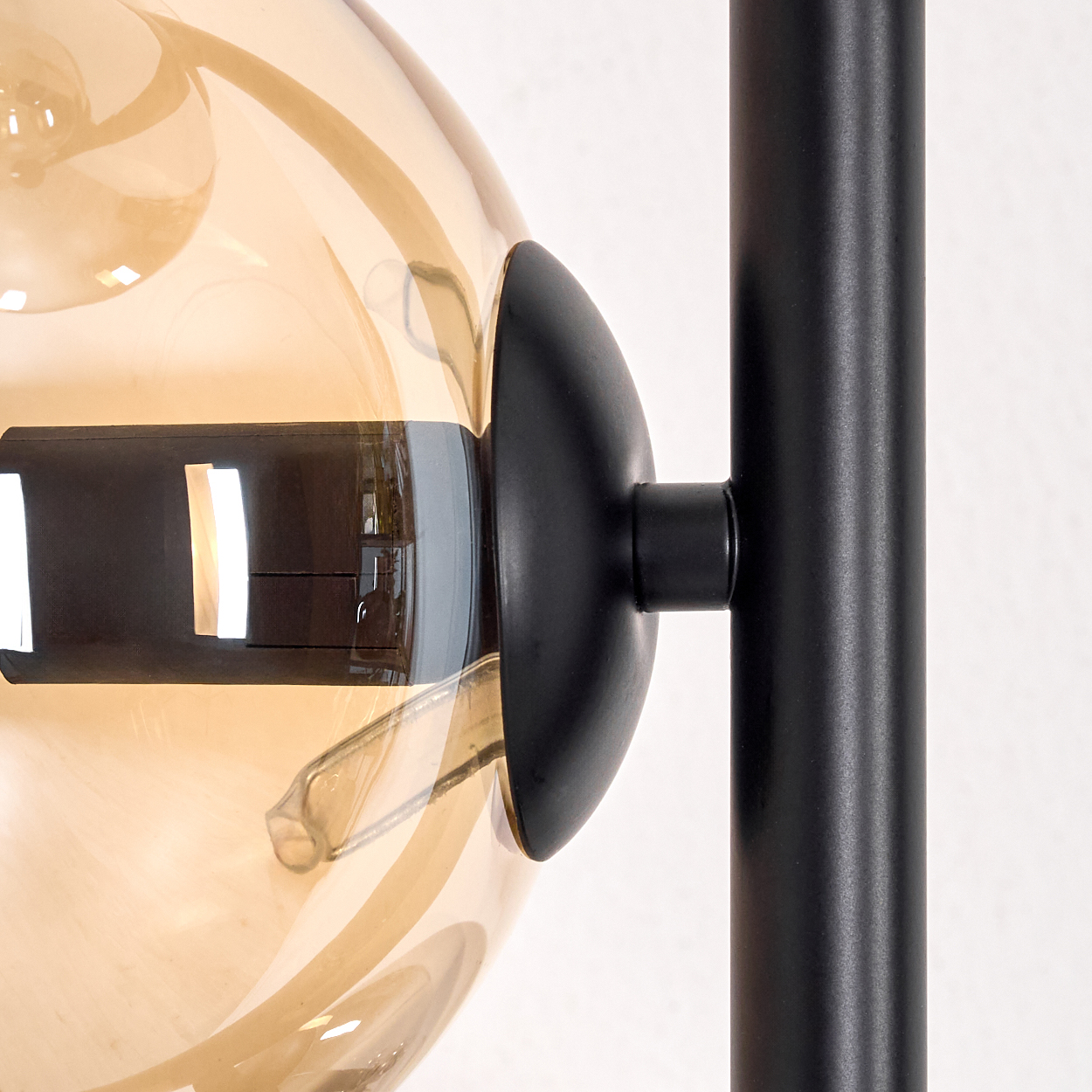 Nahaufnahme einer modernen Lampe. Eine bräunliche Glaskugel ist an einem schwarzen Metallrahmen befestigt. Der Hintergrund ist weiß.