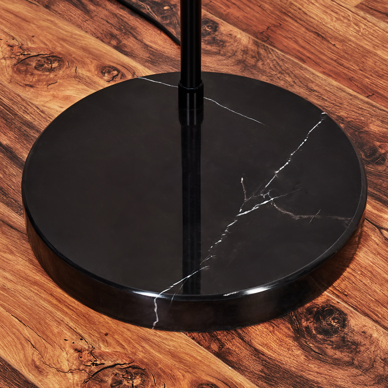 Ein schwarzer Marmor-Lampensockel steht auf einem Holzboden. Die schwarze Stange der Lampe ragt aus dem Sockel. Weiße Adern verlaufen durch den Marmor.