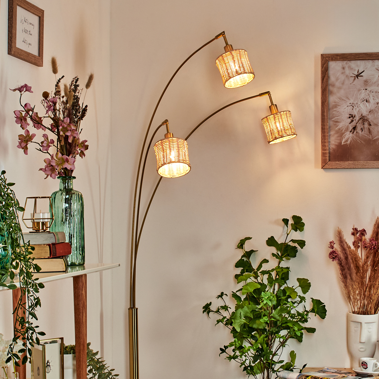 Ein Raum mit einer Stehlampe mit drei Rattanschirm, Pflanzen, Büchern und gerahmten Bildern.