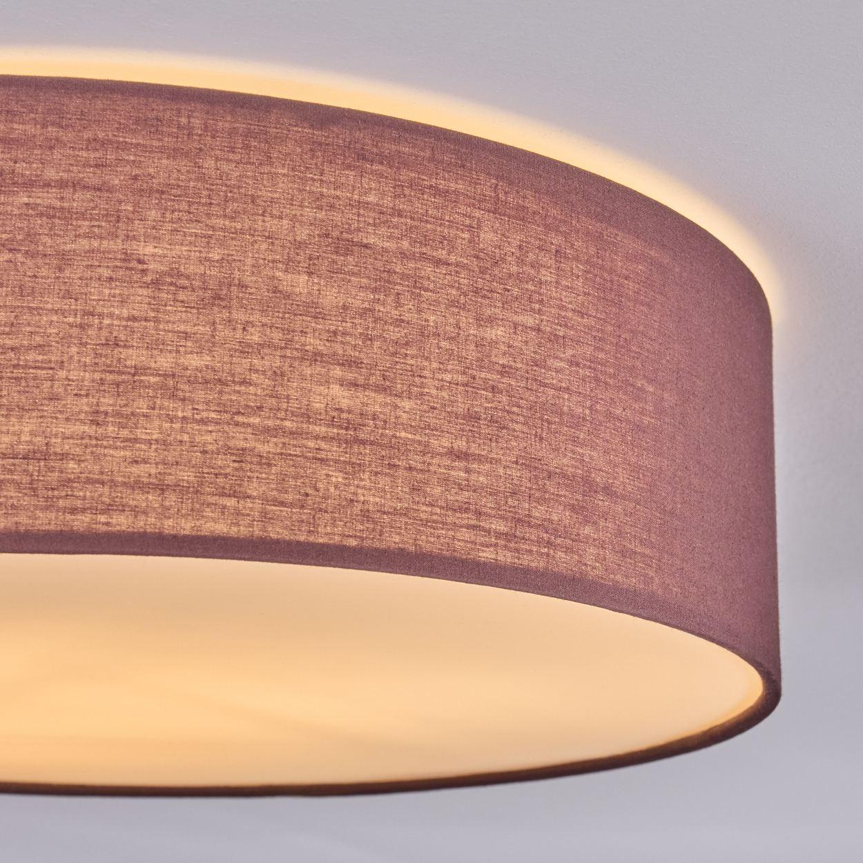 Nahaufnahme eines Lampenschirms. Der Schirm hat eine gedämpfte purpurrote Farbe mit strukturiertem Stoff. Das Licht im Inneren leuchtet warm.