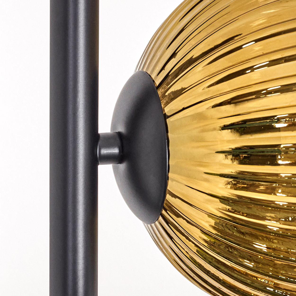 Nahaufnahme einer Lampe mit goldfarbenem, geripptem Glasschirm, der an einer schwarzen Metallstange befestigt ist.