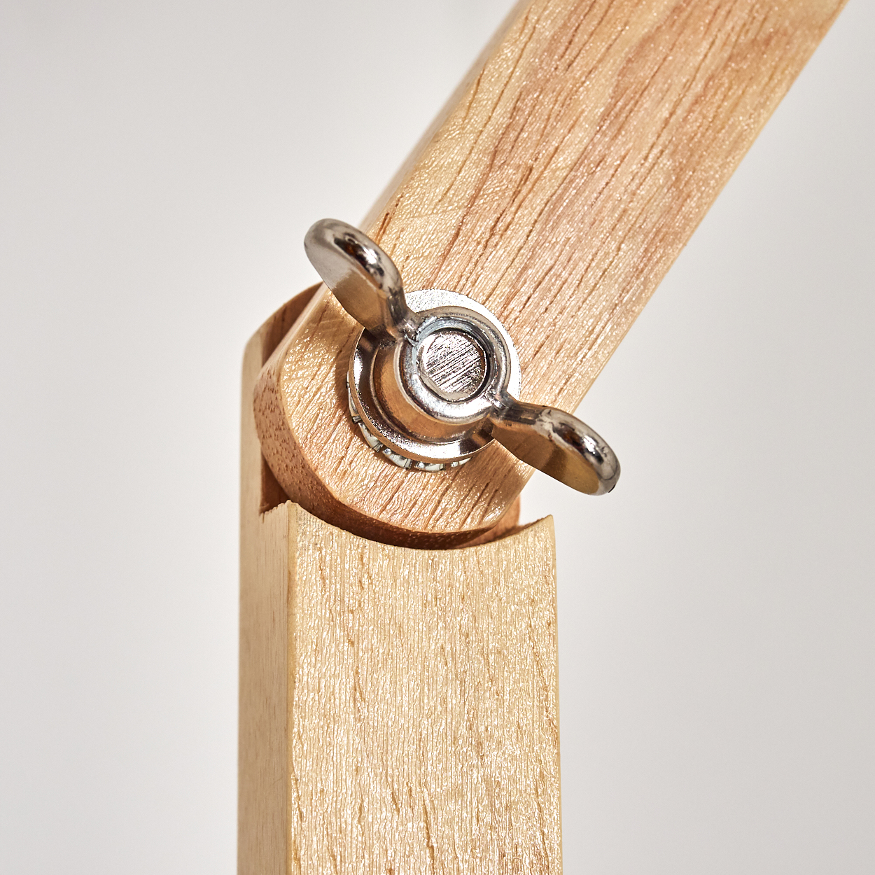 Nahaufnahme eines Holzgelenks mit einer Metall-Flügelmutter. Helles Holz vor weißem Hintergrund.