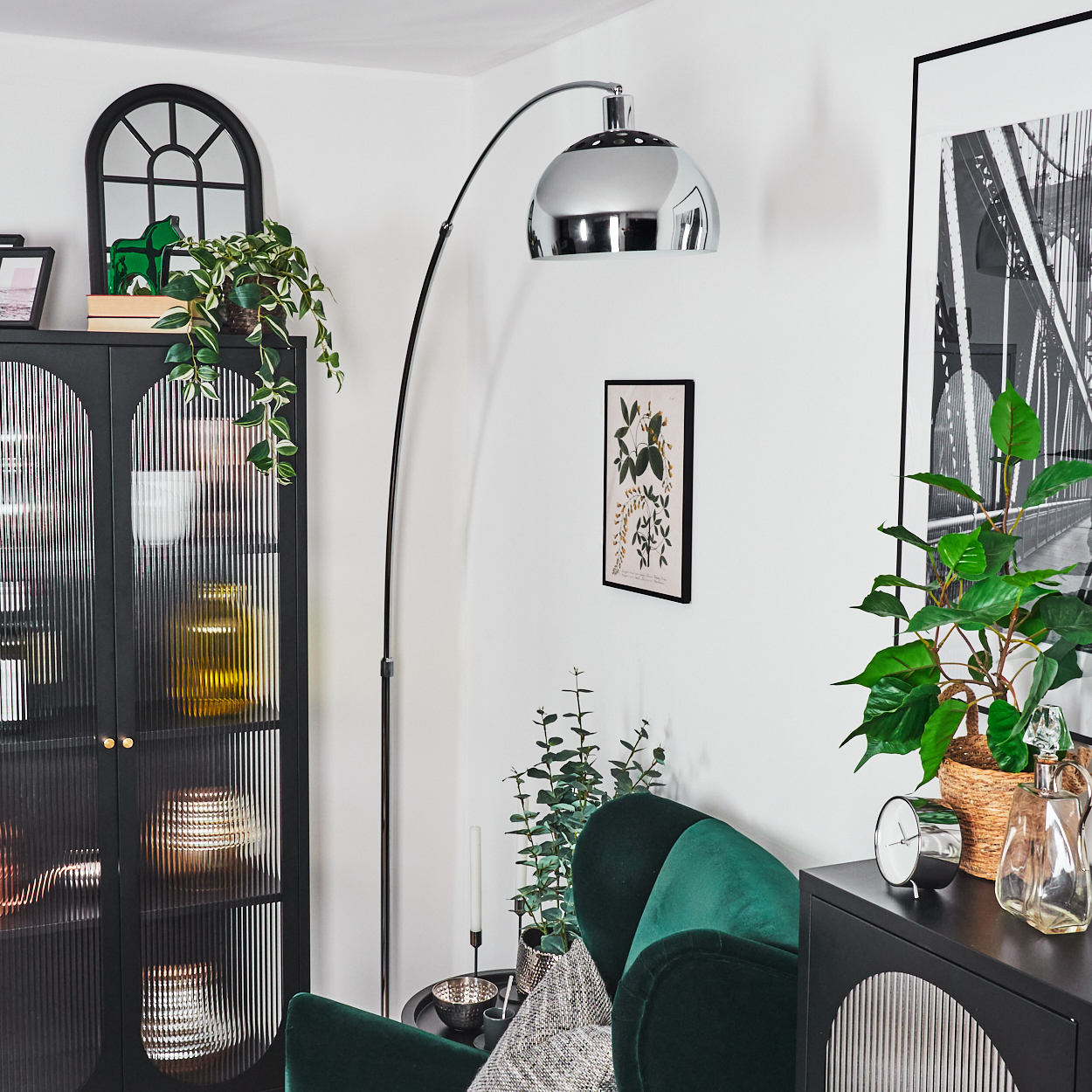 Wohnzimmerszene mit grünem Sessel, schwarzem Schrank, großer Stehlampe und Kunstwerken. Pflanzen und Dekorationen füllen den Raum.