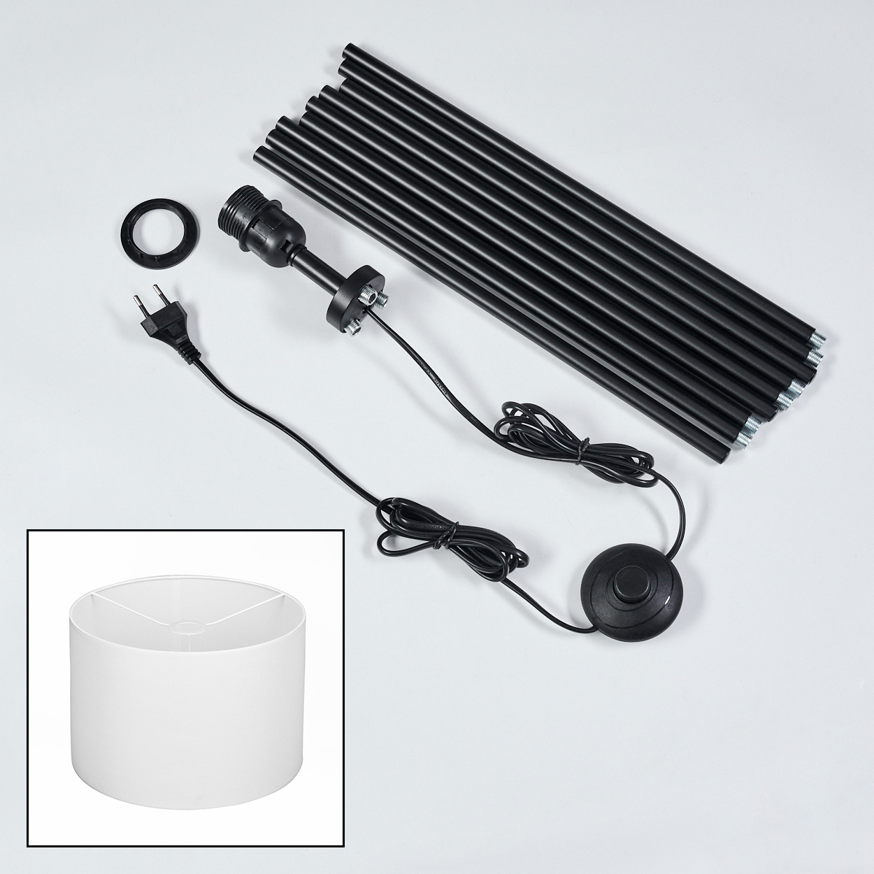 Lampenteile: schwarze Stangen, Lampenfassung, Kabel, Fußschalter, Lampenschirm. Weißer Hintergrund.
