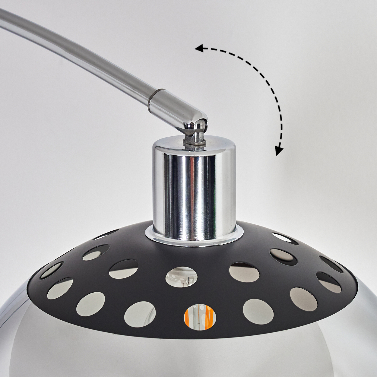 Nahaufnahme einer modernen Lampe. Sie hat einen Chromarm und -fuß, einen schwarzen perforierten Schirm und eine sichtbare Glühbirne.