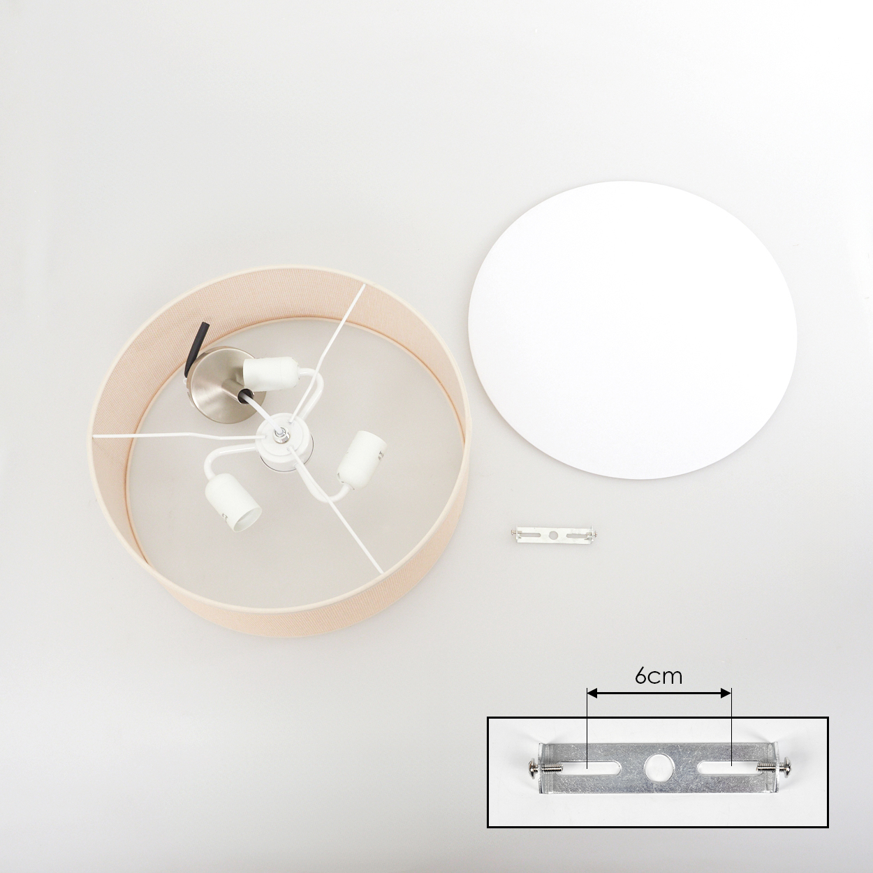 Draufsicht einer zerlegten Lampe. Beiger Lampenschirm, weiße Deckenplatte, Metallhalterung und 6cm Halterung. Alles auf weißem Hintergrund.