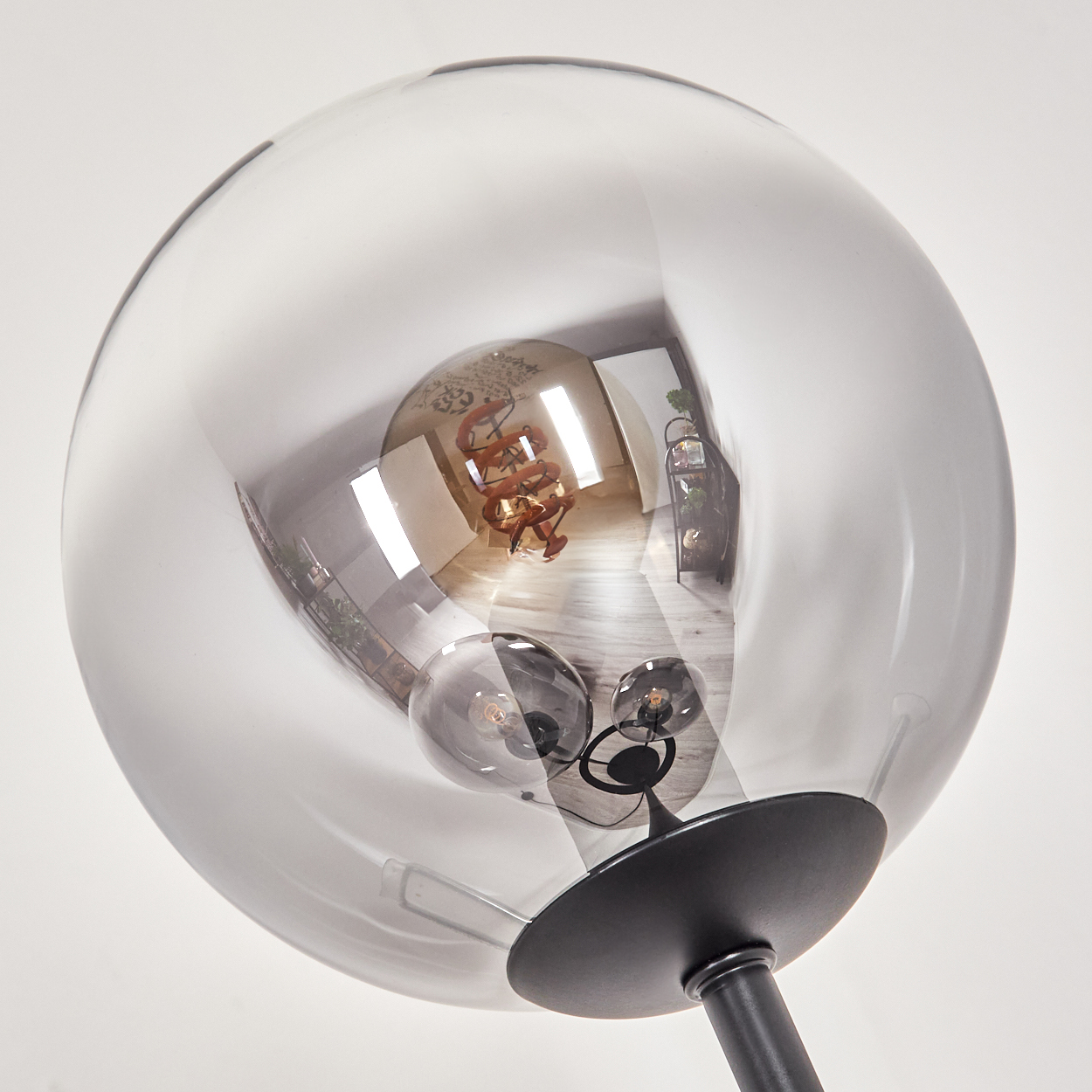 Eine moderne Lampe mit transparentem kugelförmigem Schirm, der den Raum widerspiegelt. Die Glühbirne ist sichtbar. Der Sockel ist schwarz.