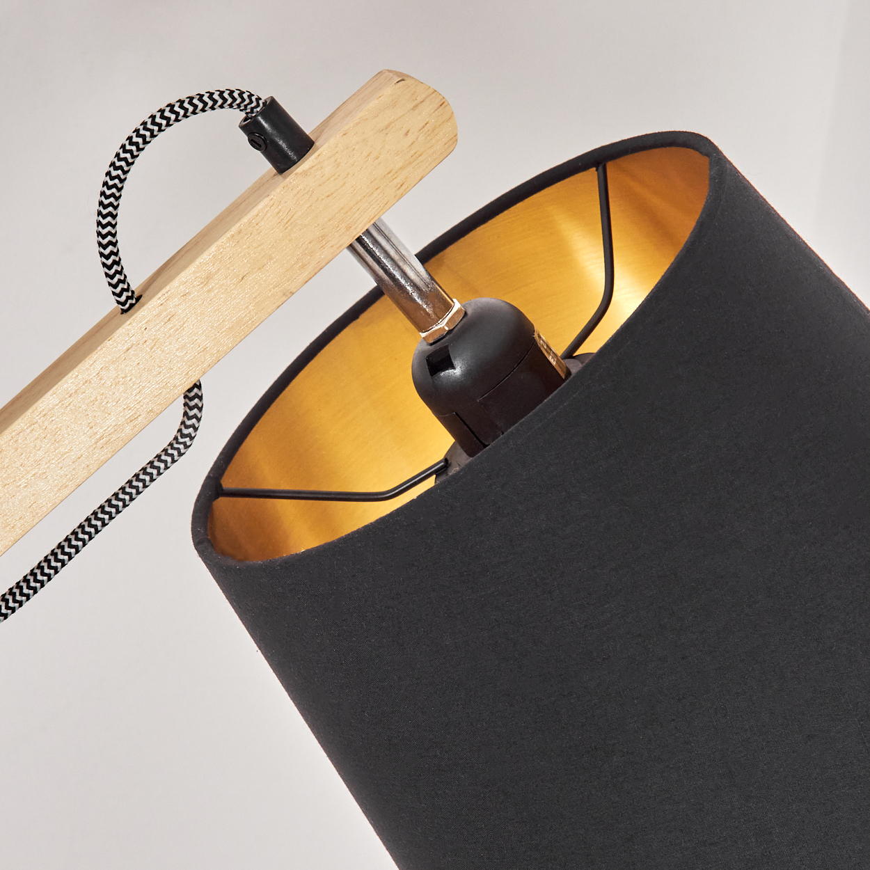 Nahaufnahme einer Lampe. Sie hat einen schwarzen Lampenschirm mit goldener Innenseite, einen Holzarm und ein schwarz-weißes Kabel.