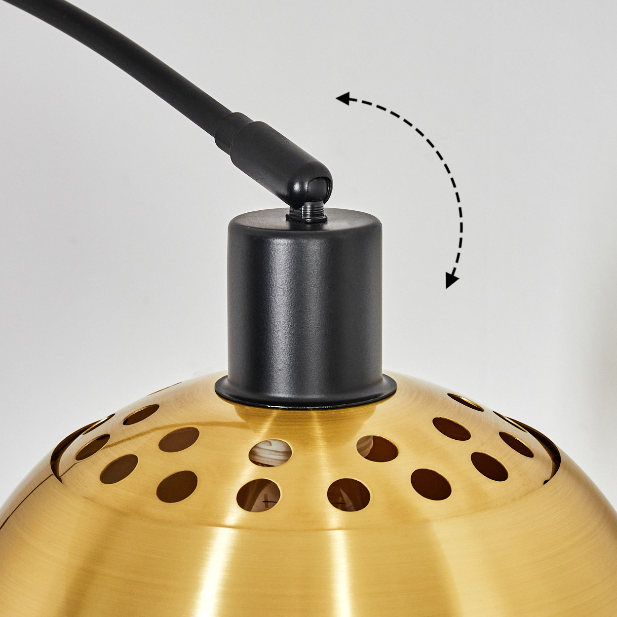 Nahaufnahme einer goldenen Lampe mit schwarzem Arm. Die Lampe hat einen perforierten Lampenschirm. Ein Pfeil zeigt die Bewegung der Lampe an.