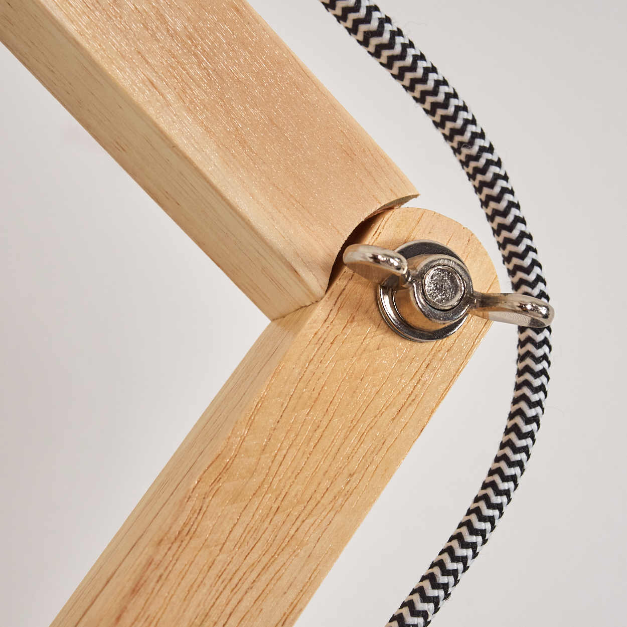 Gelenk eines Holzlampenarms mit silberner Flügelmutter. Schwarz-weißes Kabel. Helle Holzmaserung auf dem Holz.
