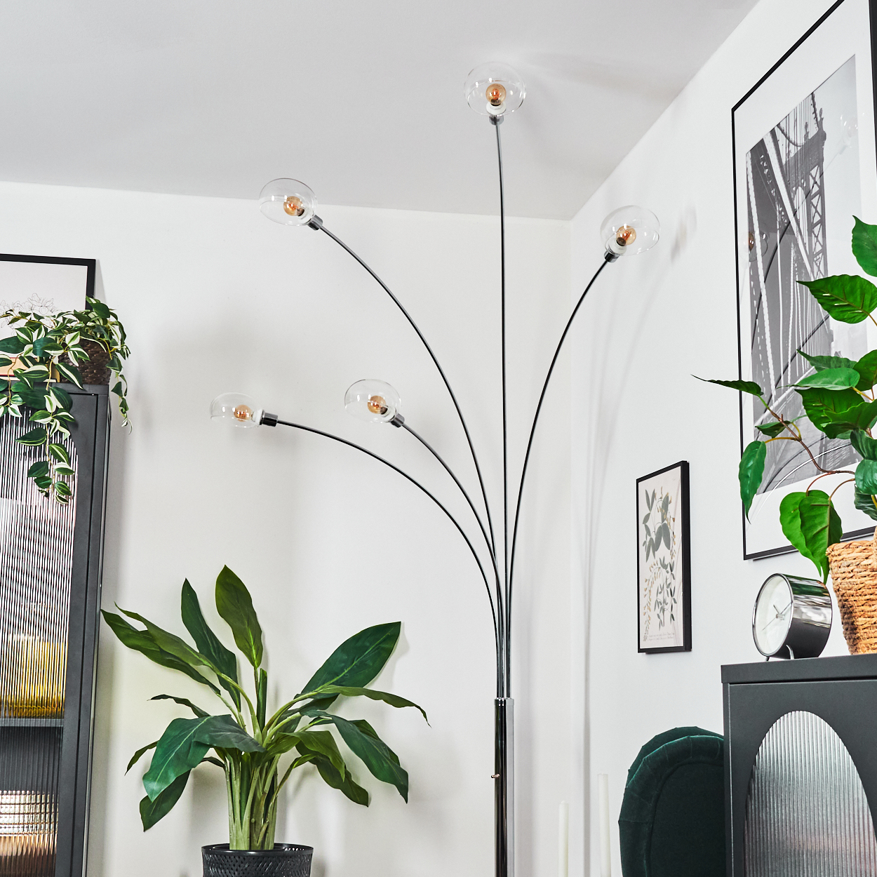 Ein modernes Wohnzimmer mit Stehlampe, Pflanzen, Kunstwerken und einem dunklen Schrank. Die Lampe hat fünf Kugelleuchten.