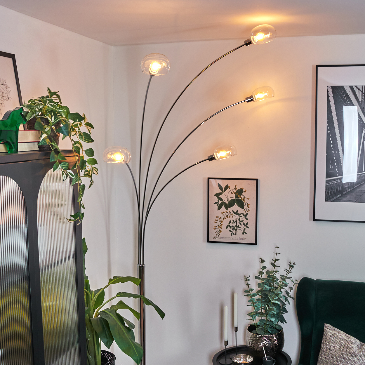 Ein modernes Wohnzimmer mit Stehlampe, Pflanzen, schwarzem Schrank und gerahmten Kunstwerken.