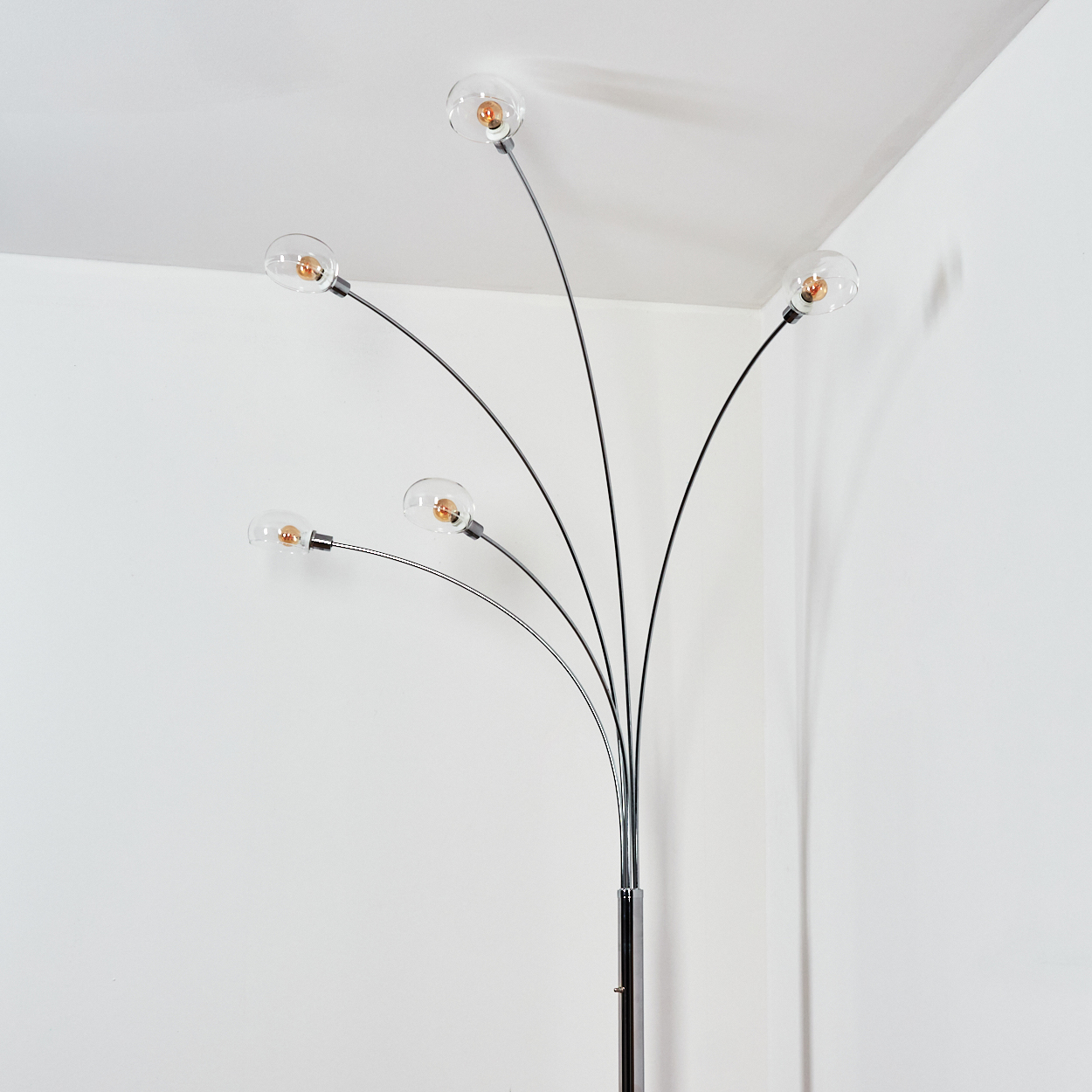 Eine moderne Stehlampe mit fünf gebogenen Armen, die jeweils eine klare Glühbirne halten. Die Lampe steht vor einer weißen Wand und Decke.