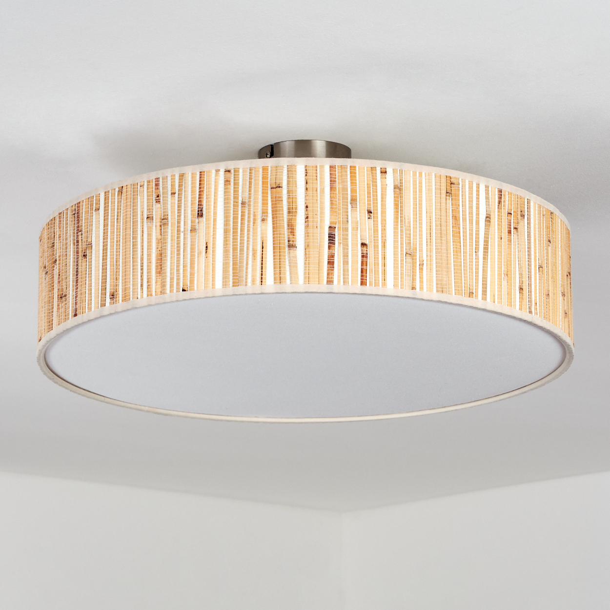 Eine runde Deckenlampe mit Bambus-Schirm und weißem Diffusor. Der Hintergrund ist eine weiße Decke.