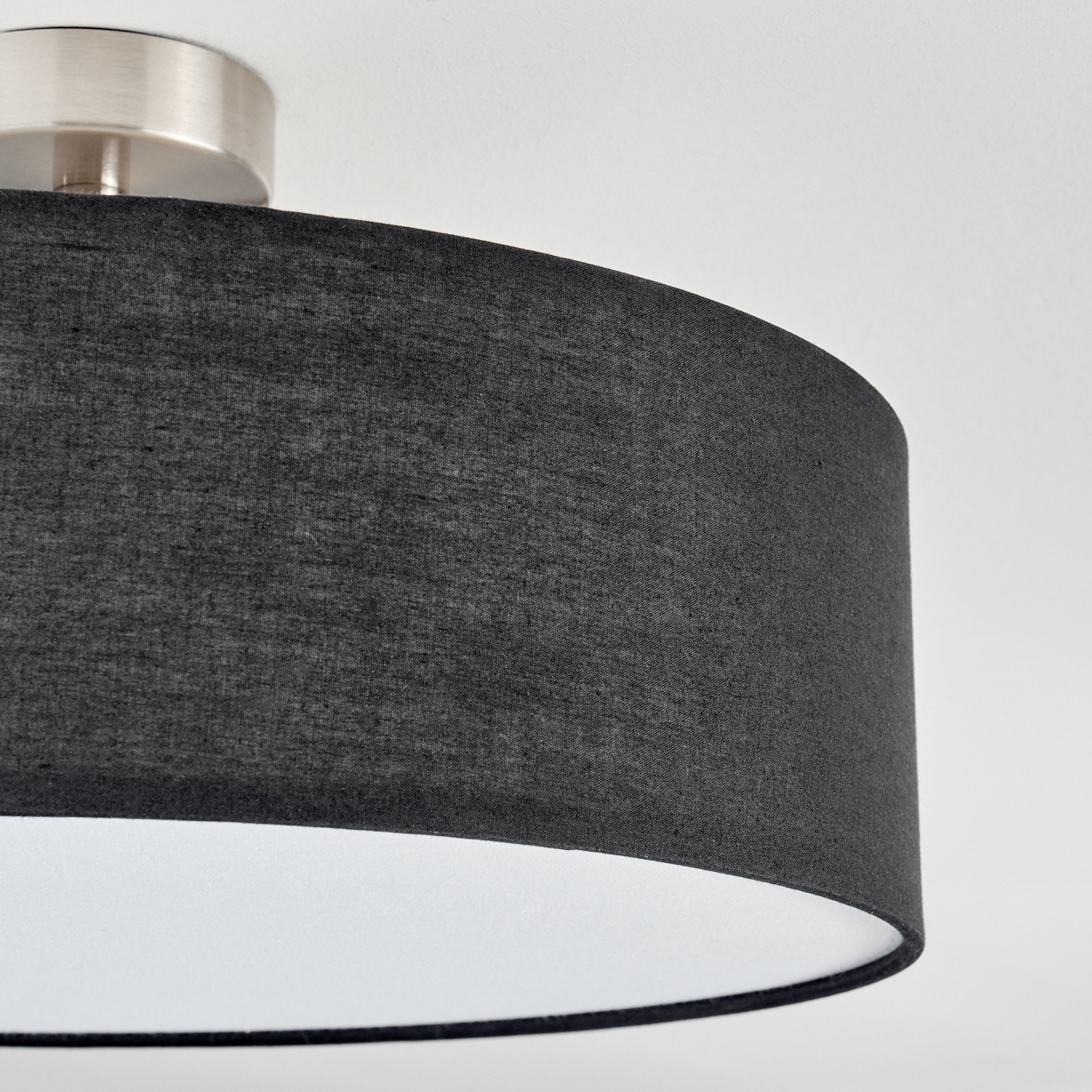 Nahaufnahme einer Deckenlampe. Sie hat einen dunkelgrauen Schirm und einen silbernen Sockel. Der Hintergrund ist weiß.