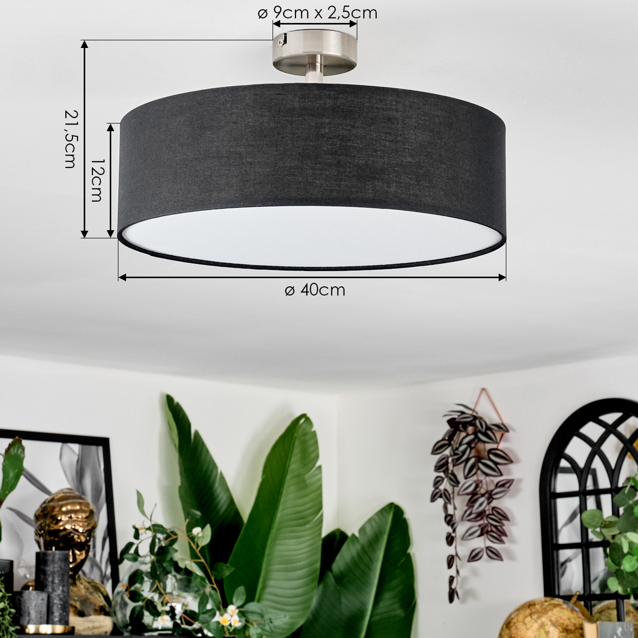 Dunkelgraue Deckenlampe mit Maßangaben. Die Lampe befindet sich über grünen Pflanzen und einem gerahmten Bild.