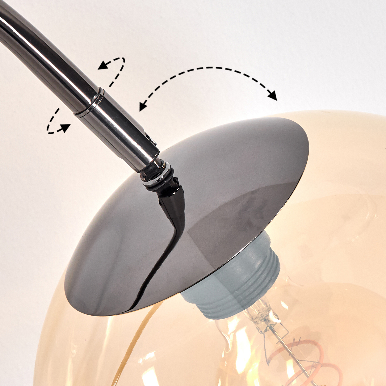 Nahaufnahme einer Lampe mit Chromarm und schwarzem Schirm. Die Glühbirne ist in klarem, orangefarbenem Glas eingeschlossen.