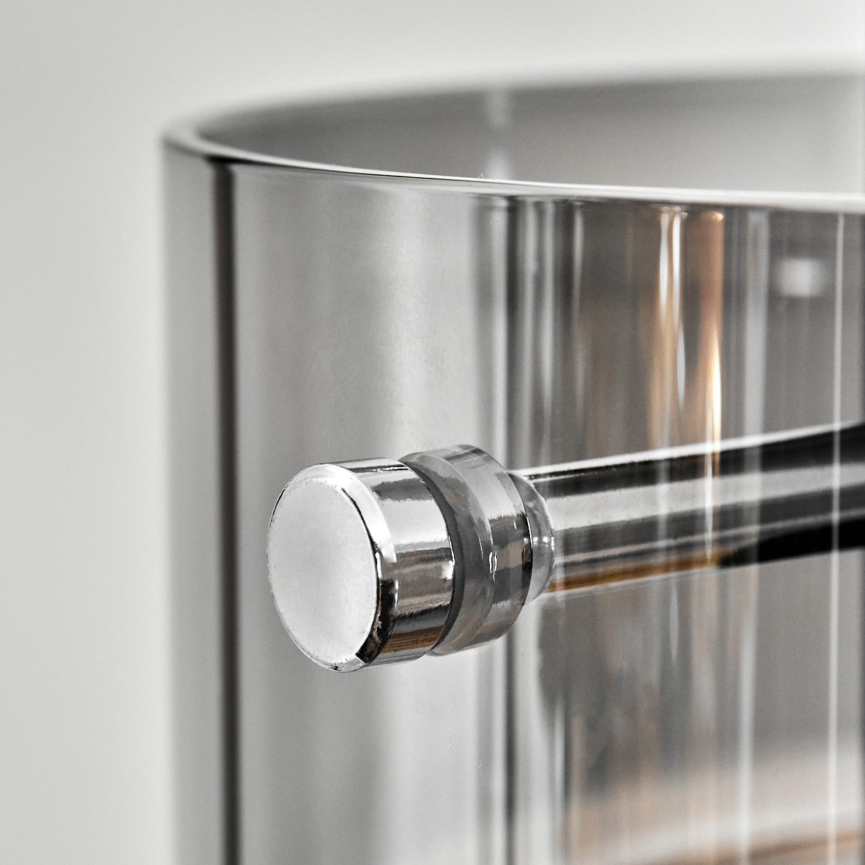 Nahaufnahme eines Glasbehälters mit einem Metallgriff. Der Griff ist rund und hat eine glänzende, reflektierende Oberfläche. Der Behälter ist klar.