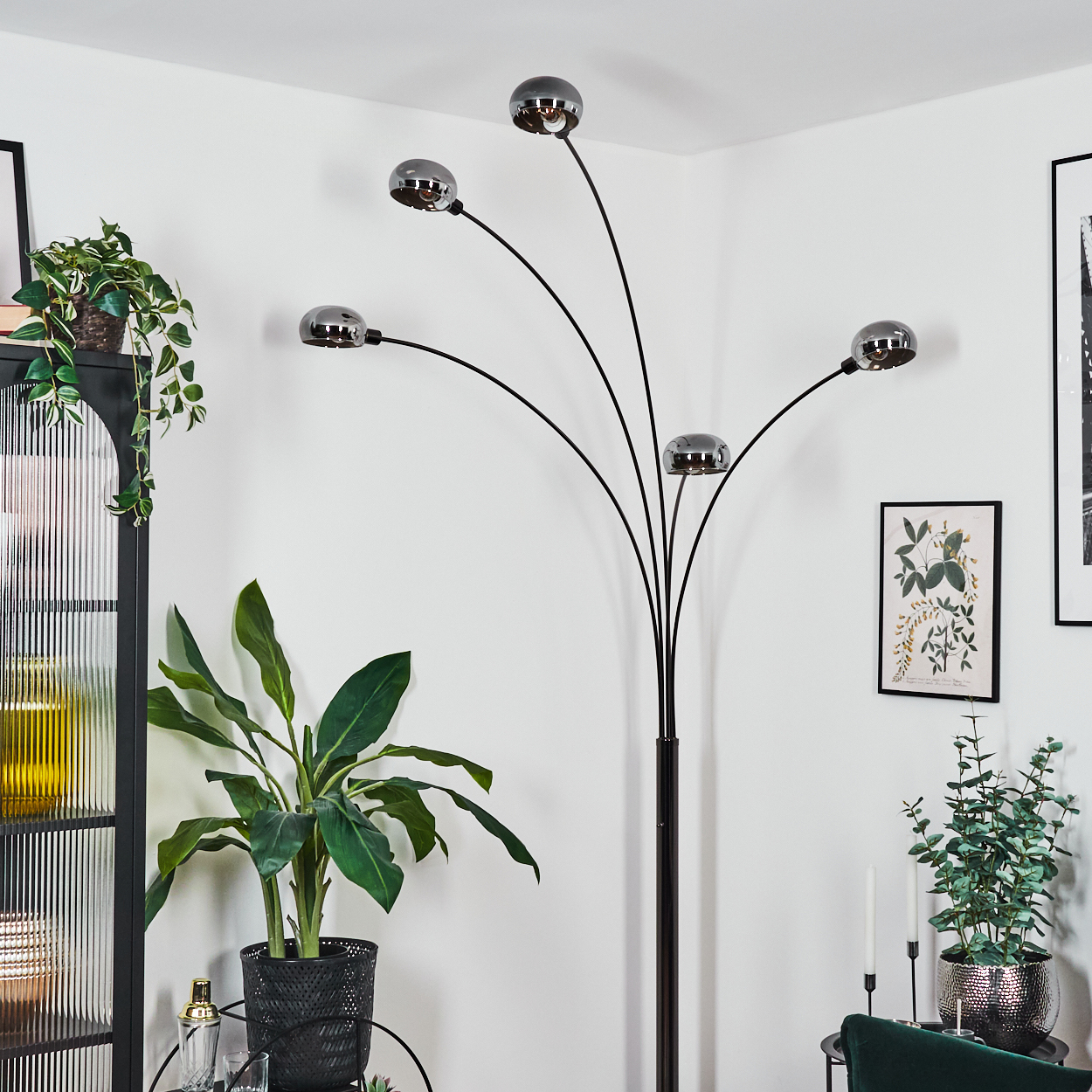 Ein modernes Wohnzimmer mit einer schwarzen Stehlampe mit fünf Lichtern. Pflanzen, Bilder und Möbel vervollständigen die Szene.
