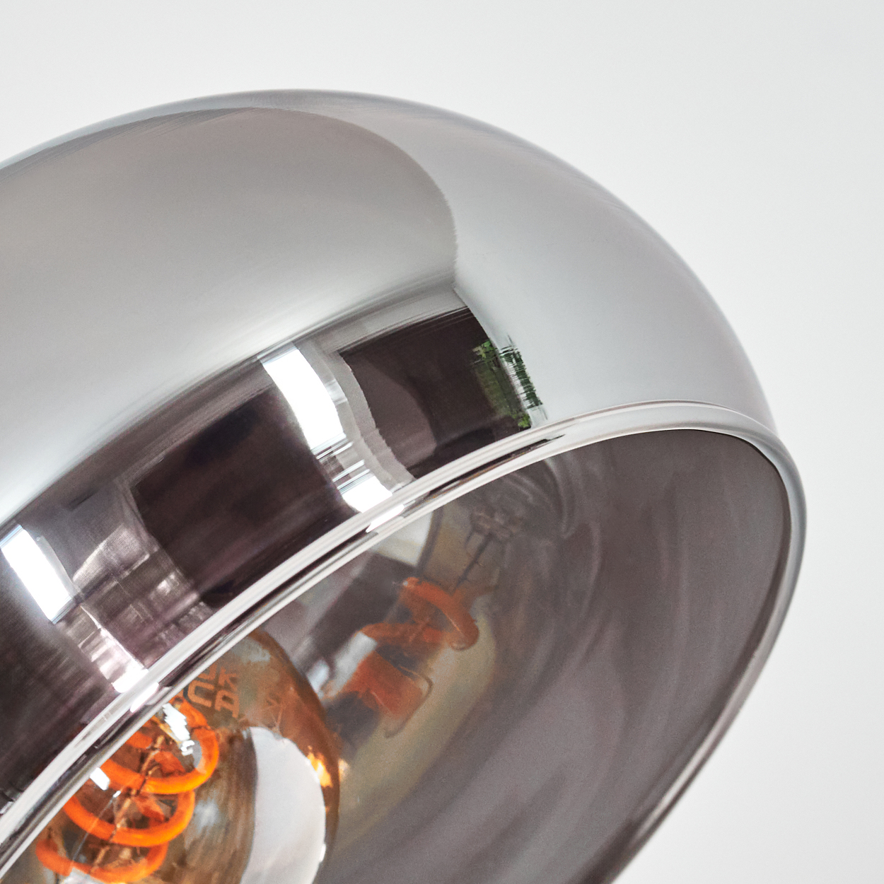 Nahaufnahme einer Chromlampe. Die Lampe reflektiert Licht und zeigt die Glühbirne im Inneren. Der Hintergrund ist weiß.