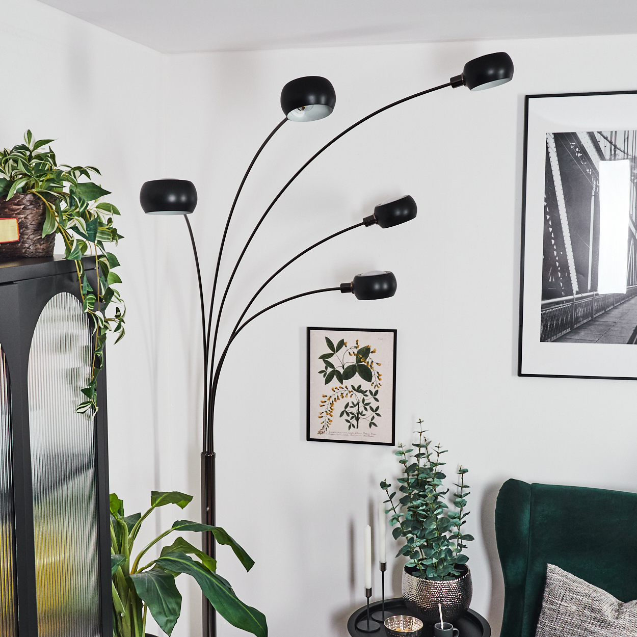 Ein modernes Wohnzimmer mit schwarzer Lampe, Pflanzen, einem Bild und einem grünen Sessel. Der Hintergrund ist weiß.