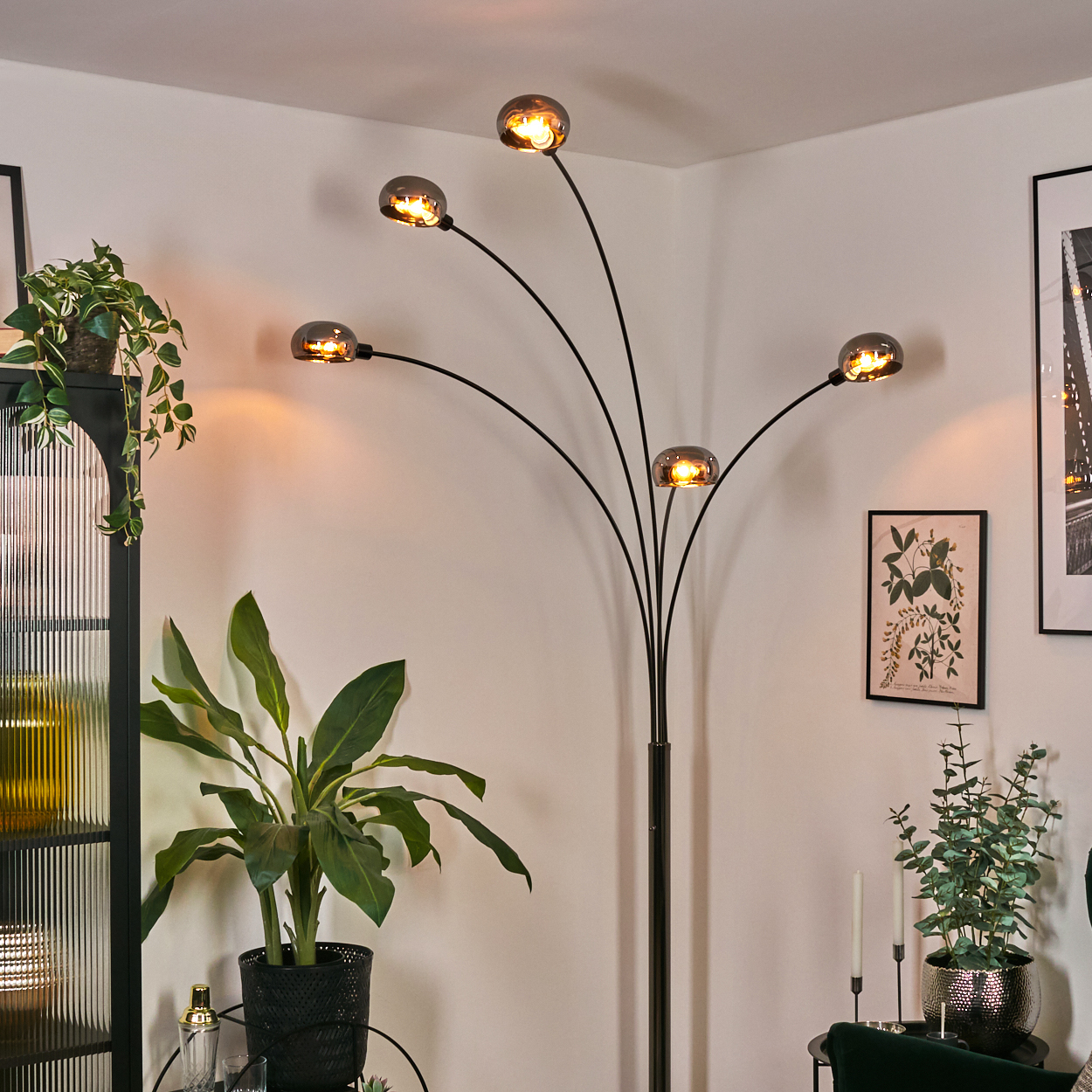 Eine moderne Stehlampe mit fünf Lichtern, Pflanzen und ein gerahmtes Bild schmücken die Ecke eines Raumes und schaffen eine gemütliche Atmosphäre.